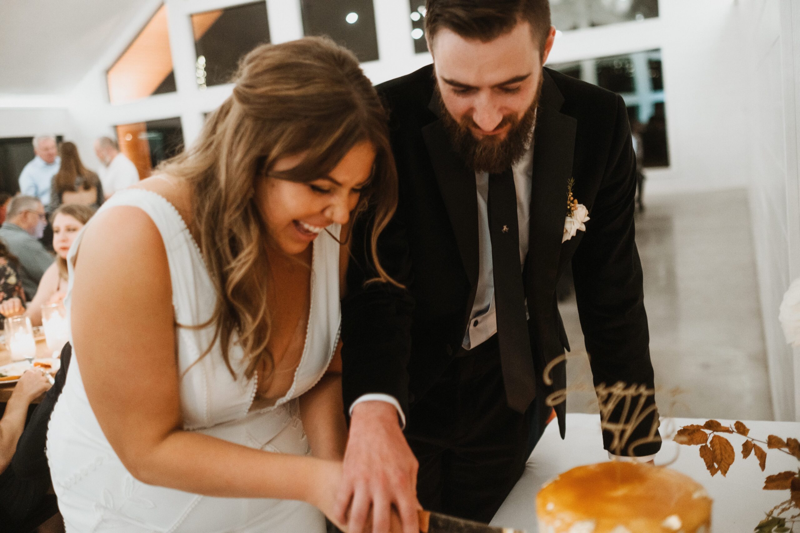 A bride and groom cut a cake together against a white venue interior. Photographed at a La Pointe Events Wedding