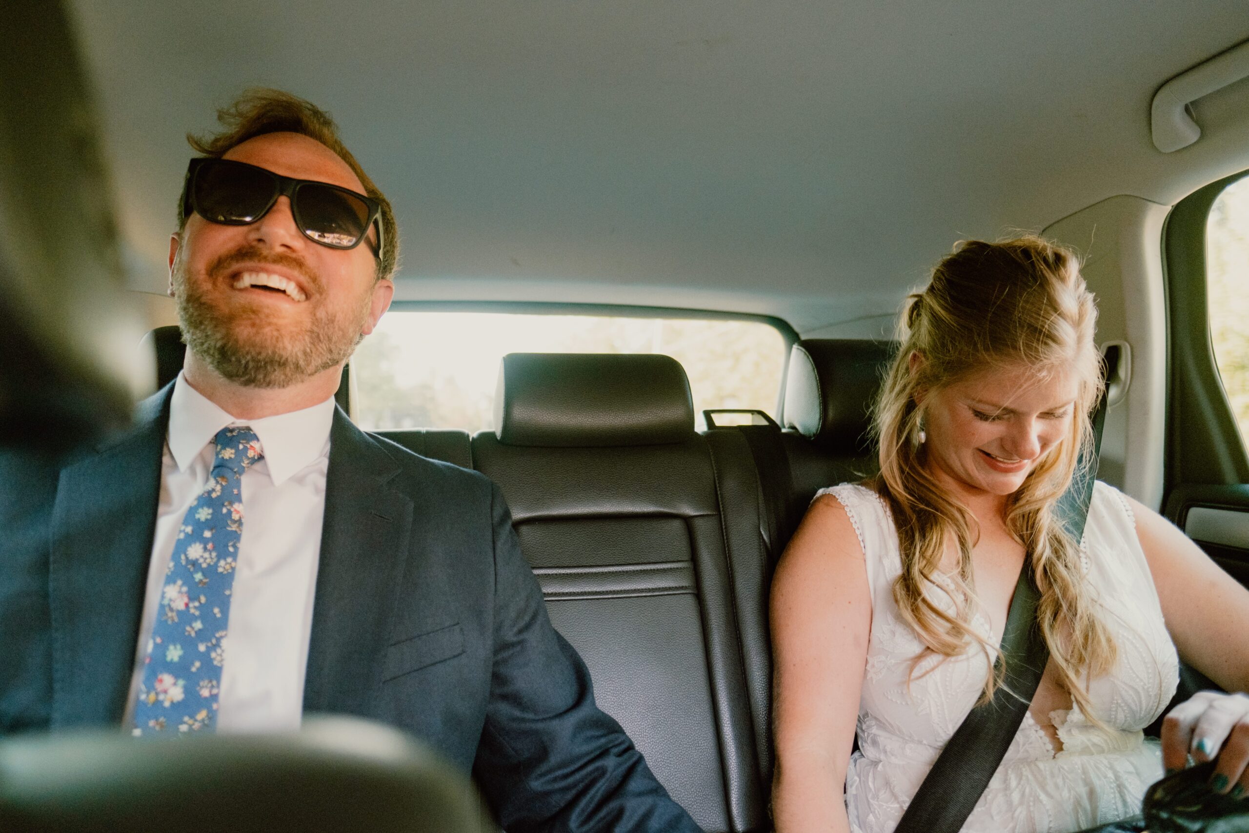 bride and groom laugh and hold hands in backseat of car on the way to their park point beach house wedding