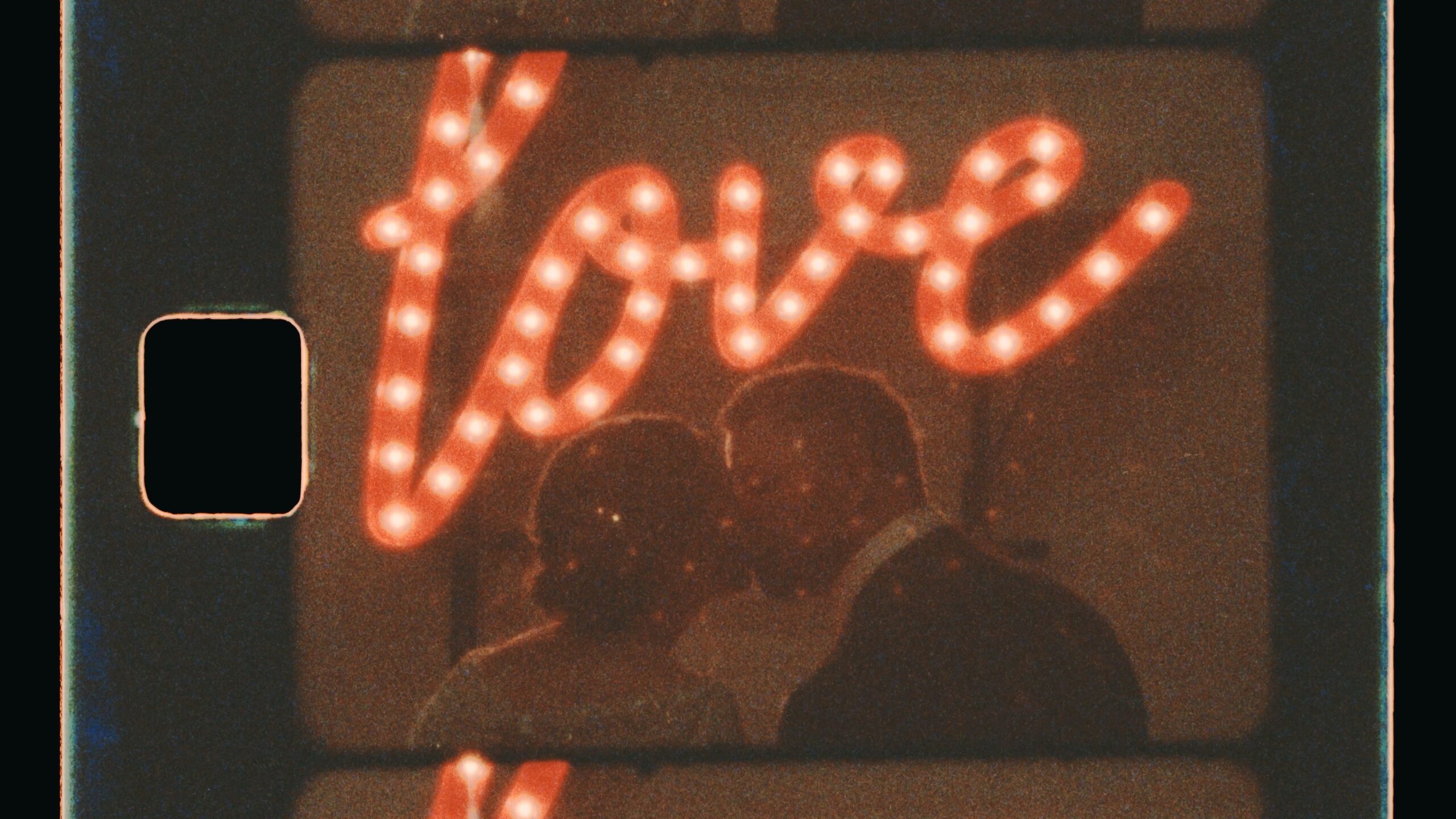 a couple kisses in front of a "love" marquee sign